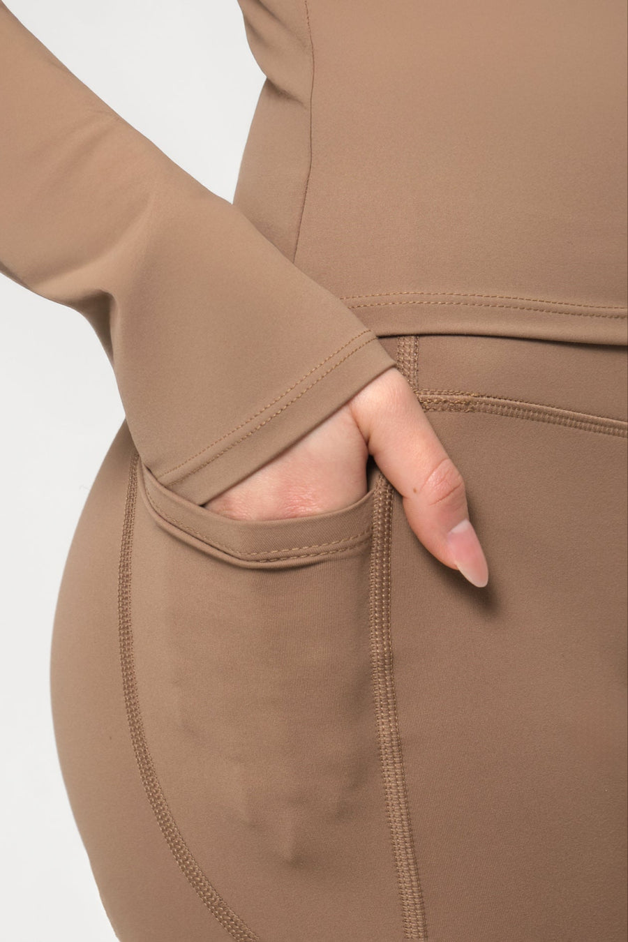 Brown long-sleeve top with a hand in the pocket on a light gray background