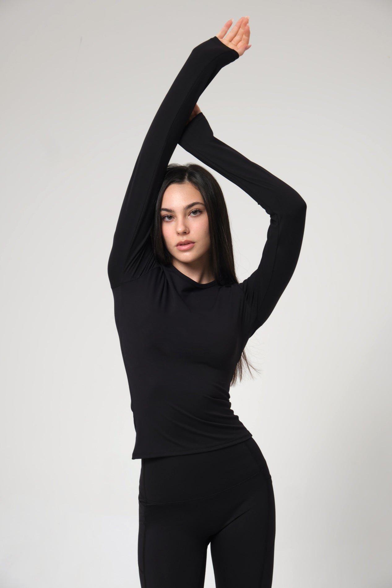 Woman wearing a black long-sleeve top and black pants against a white background