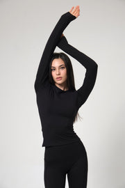 Woman wearing a black long-sleeve top and black pants against a white background
