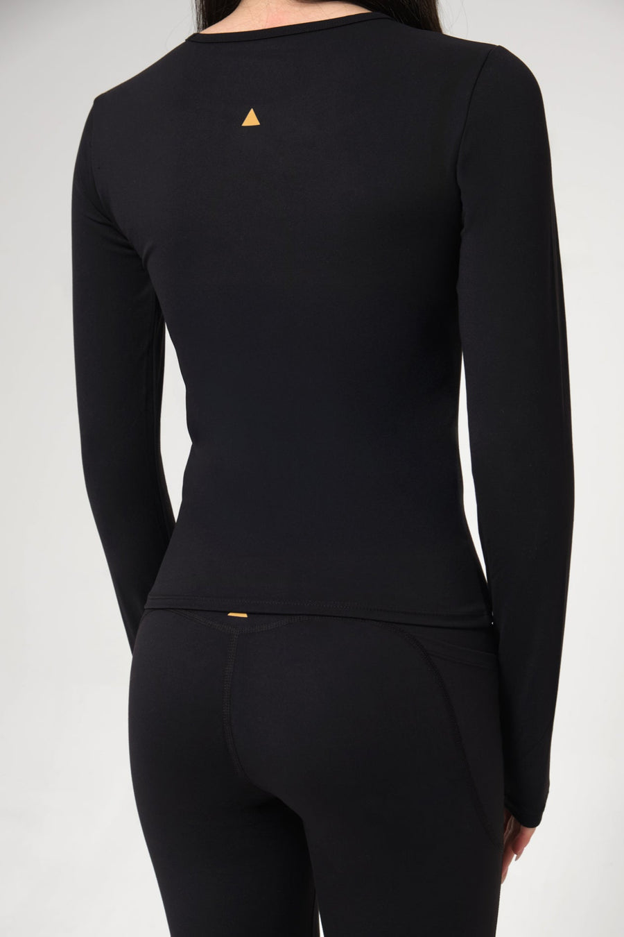 Black long-sleeve top with a small yellow triangle logo on a gray background