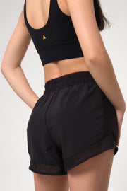 Woman wearing black athletic shorts and sports bra on a light gray background