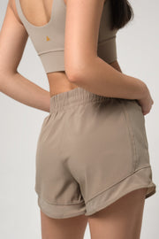 Woman wearing beige athletic shorts and sports bra on a plain background