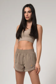 A female model wearing a matching set of beige sports bra and shorts, standing against a plain background.