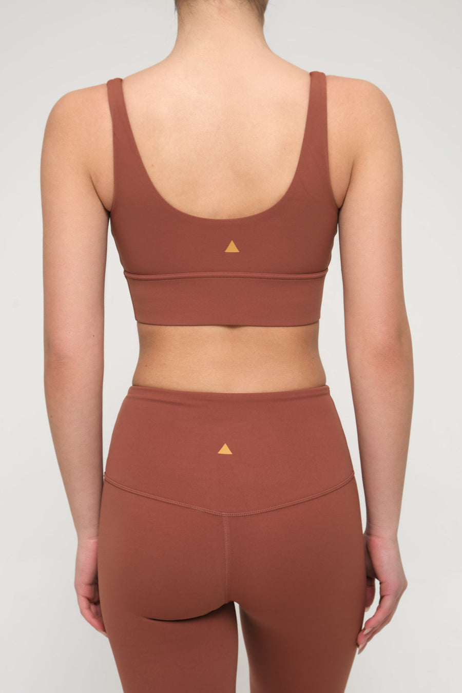 Brown sports bra and leggings set with a triangle logo on a plain background