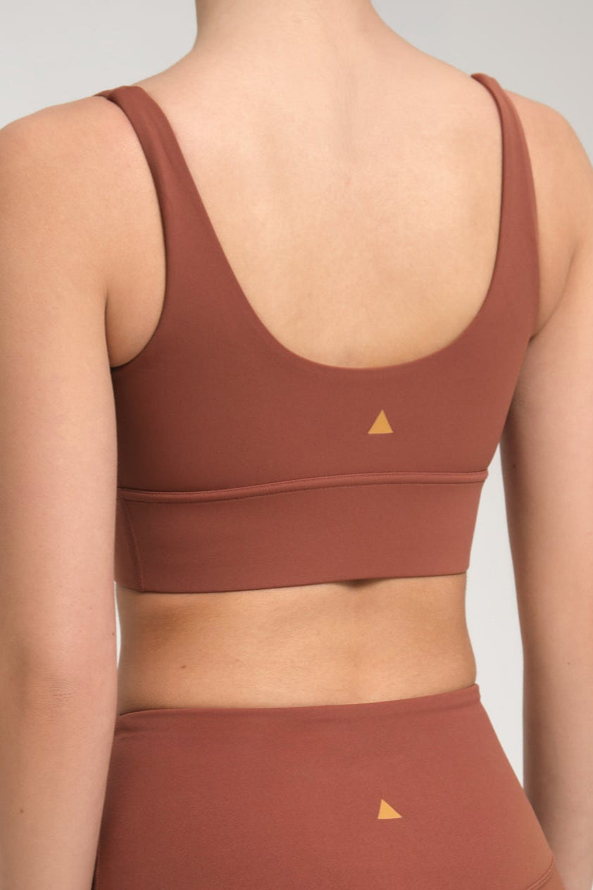 Brown sports bra and leggings with a triangle logo on a plain background