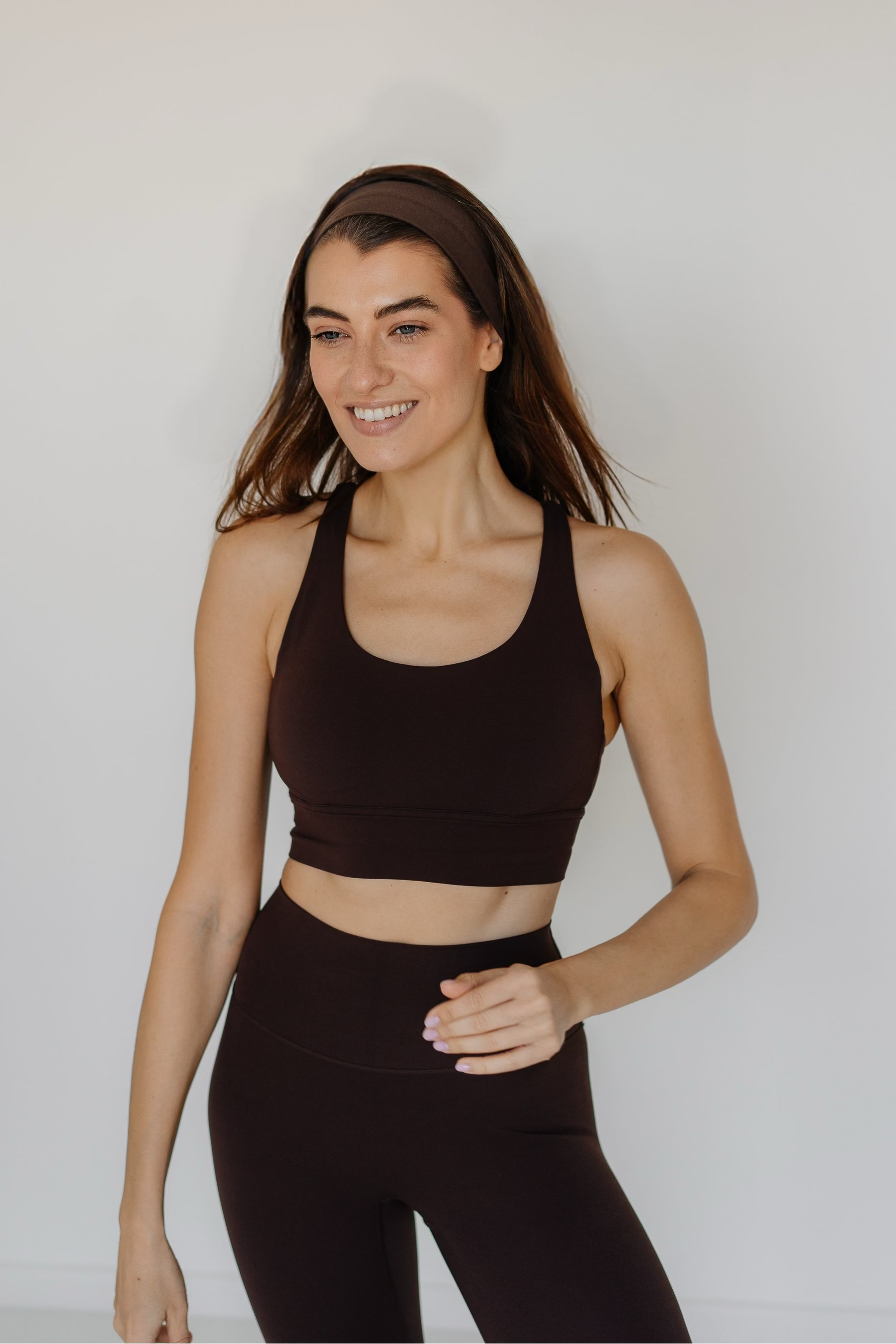 Woman wearing a dark brown sports bra and leggings against a plain background