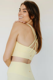 Woman wearing a light yellow strappy top against a plain background