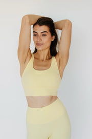 Woman wearing a yellow sports bra and leggings against a white background