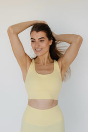 Woman wearing a yellow sports bra and leggings against a white background