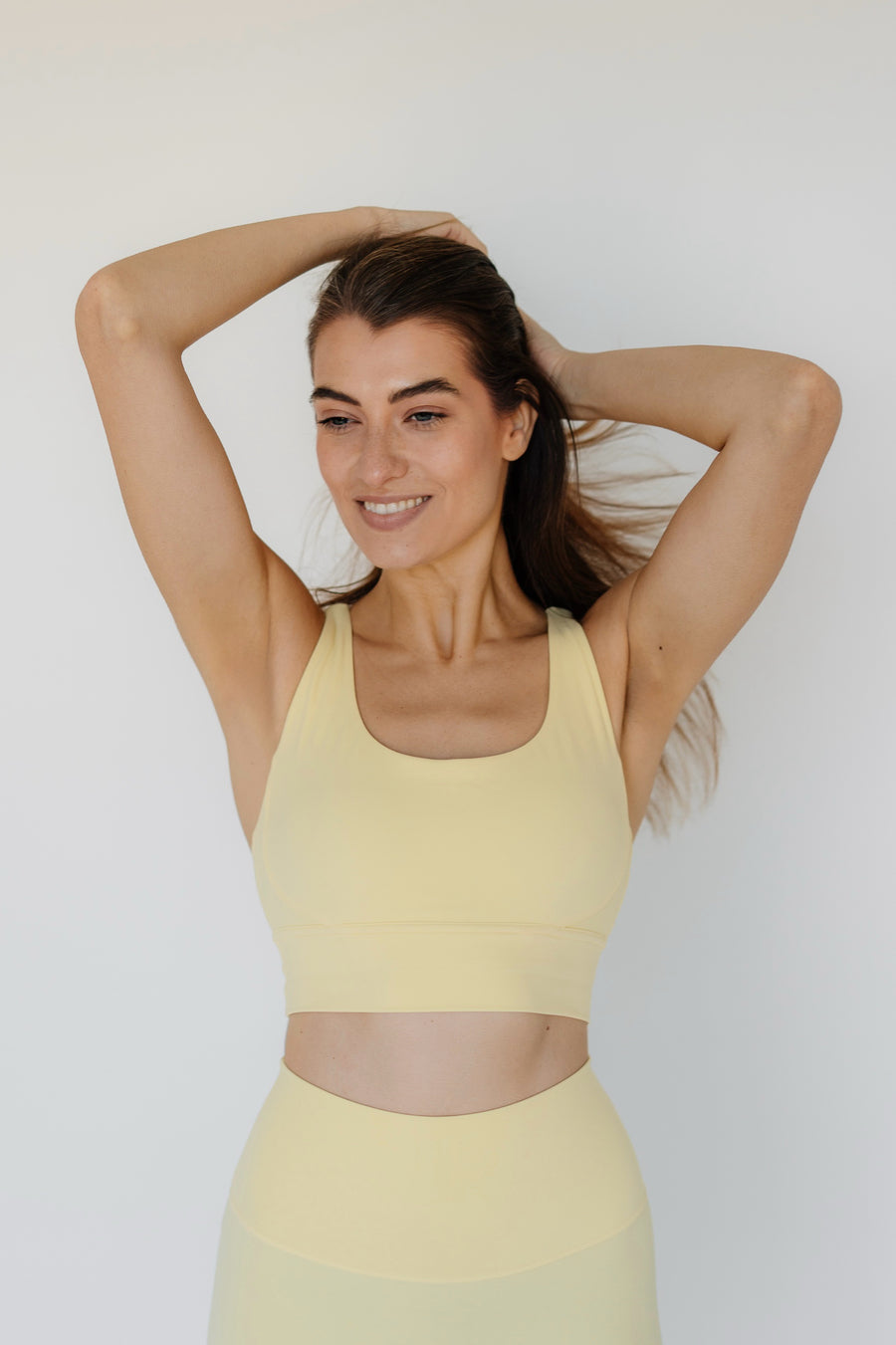 Woman wearing a yellow sports bra and leggings against a white background