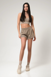 Woman wearing a beige sports bra and shorts set on a white background