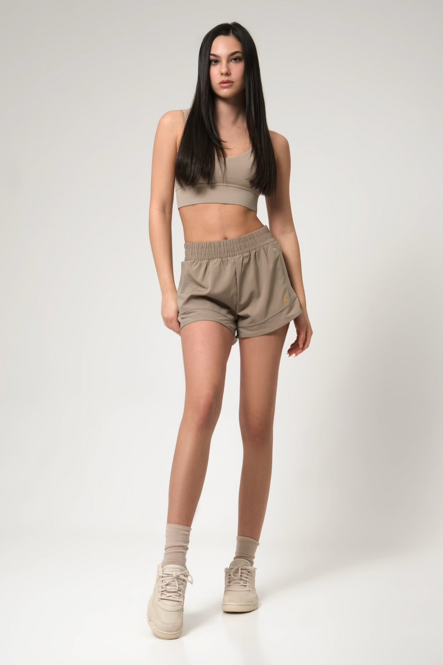 Woman wearing a beige sports bra and shorts set on a white background