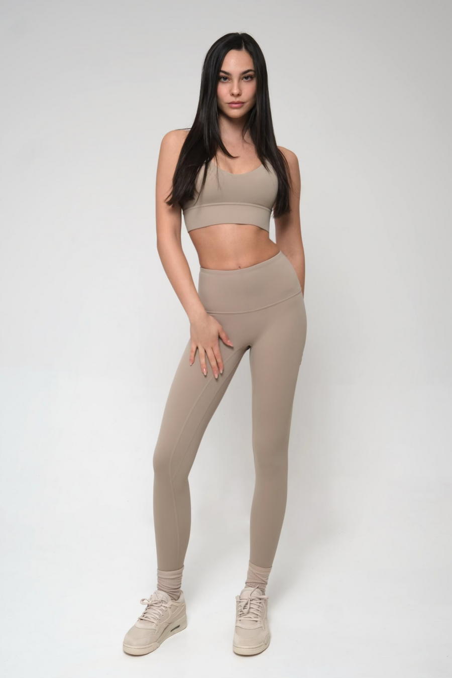 Woman wearing a beige sports bra and leggings set on a white background