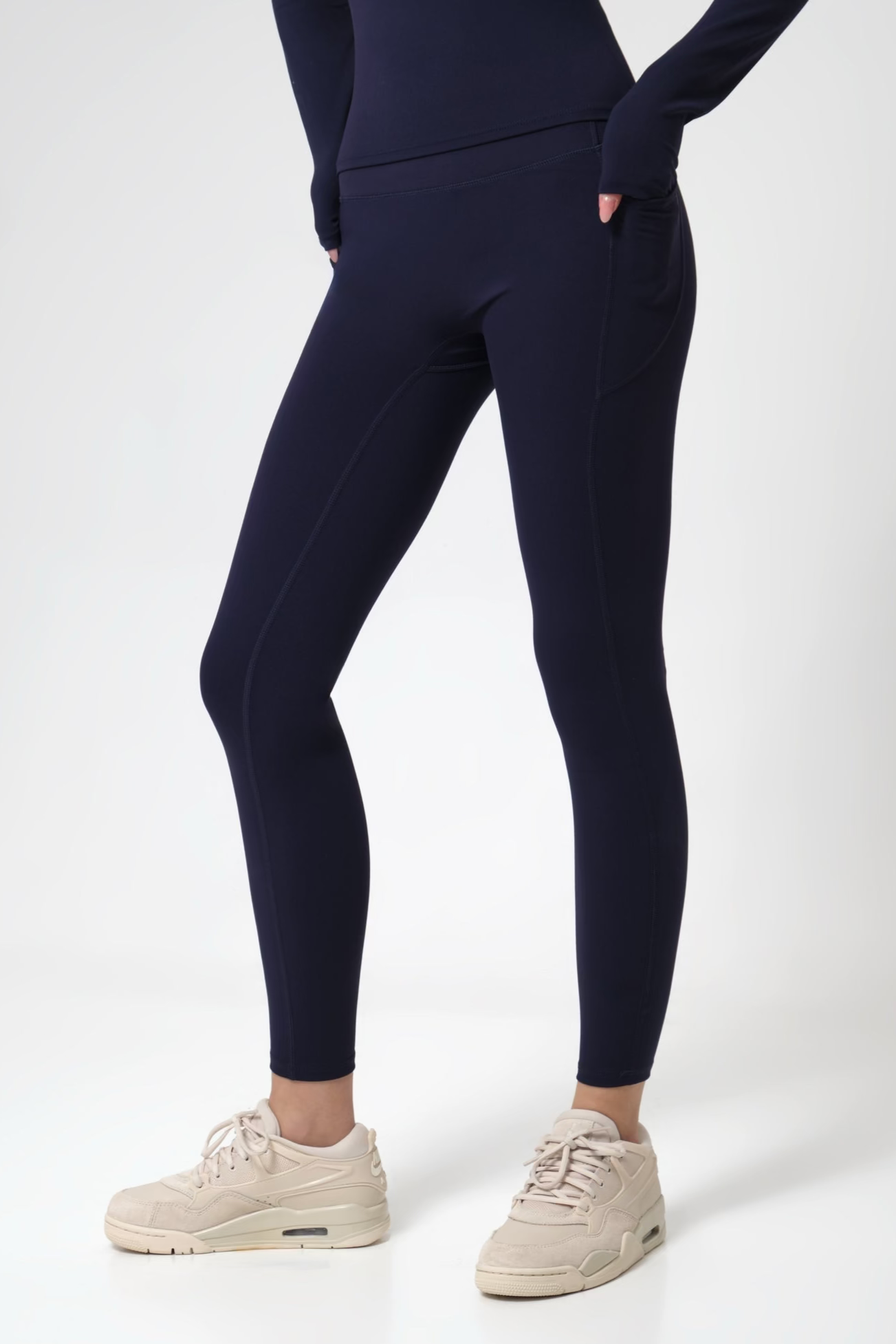 Woman wearing navy leggings and white sneakers on a white background