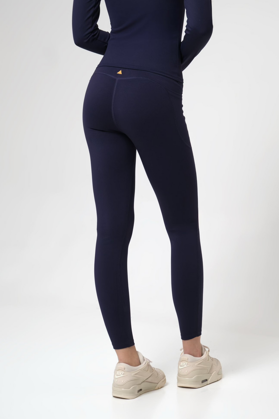 Woman wearing navy leggings and a matching top on a white background