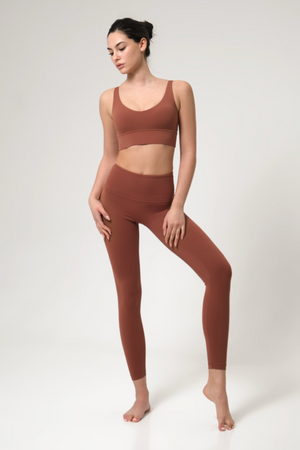 Woman wearing a brown sports bra and leggings set on a white background
