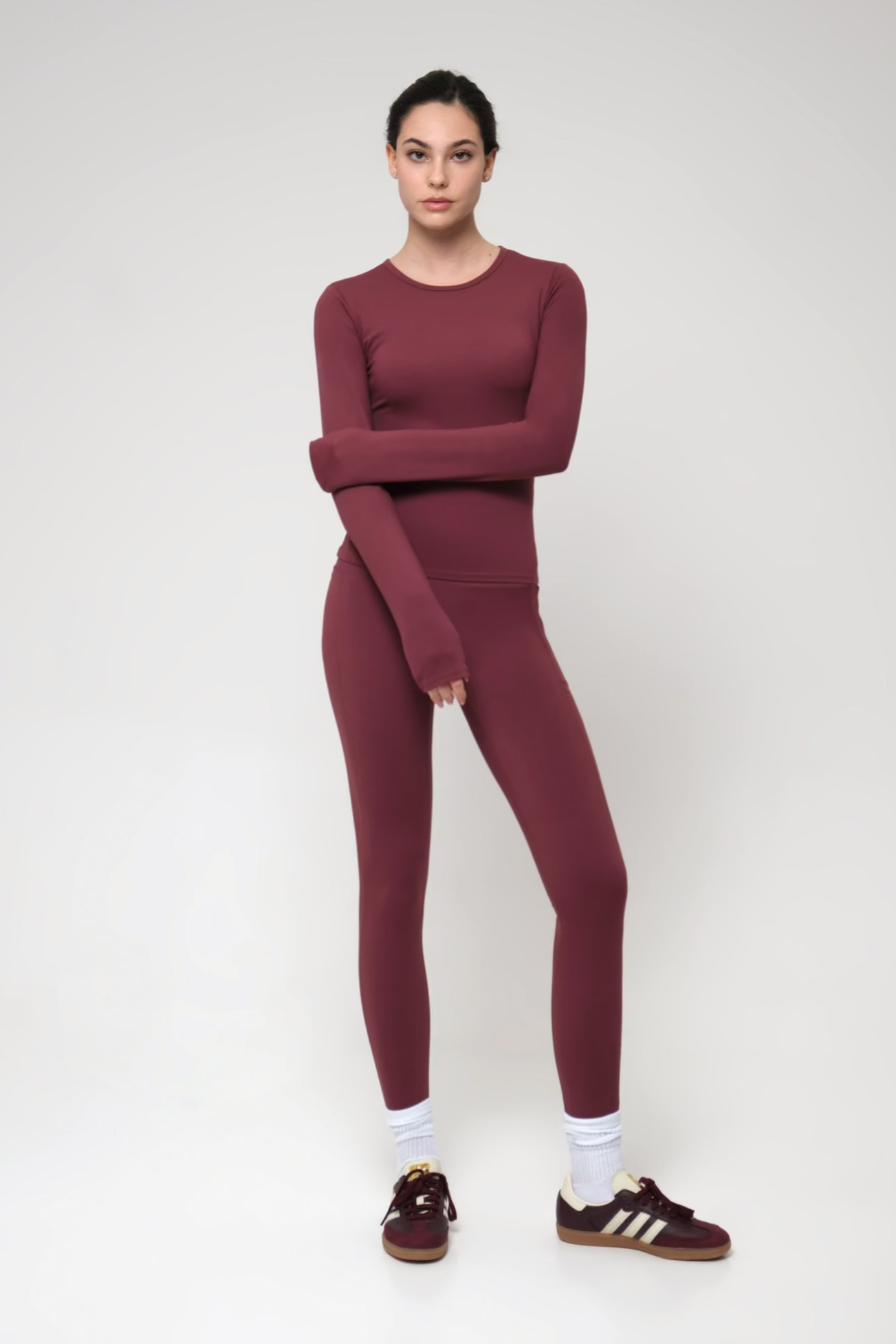 Woman wearing a burgundy outfit with Adidas shoes on a white background
