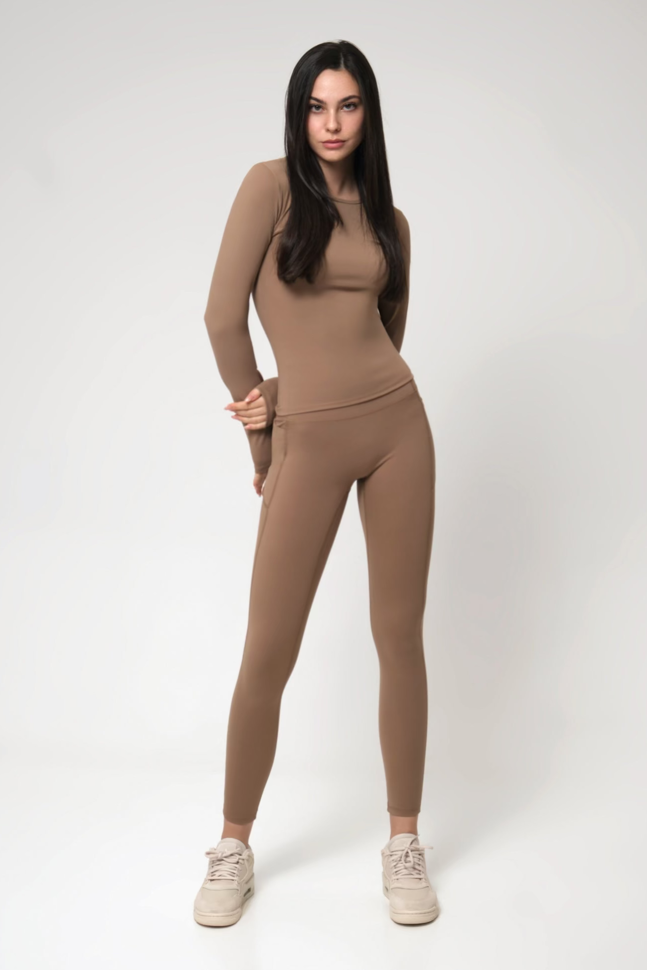 Woman wearing a brown long-sleeve top and leggings on a white background