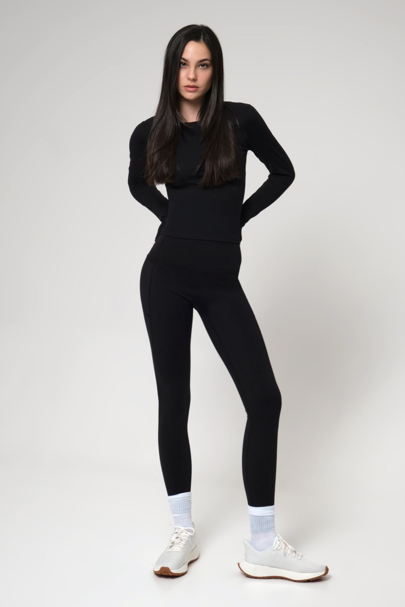 Woman wearing a black outfit with white sneakers on a plain background