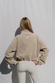 Person wearing a beige jacket with a logo on a plain background