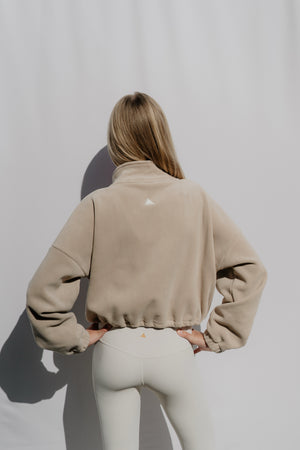 Person wearing a beige jacket with a logo on a plain background