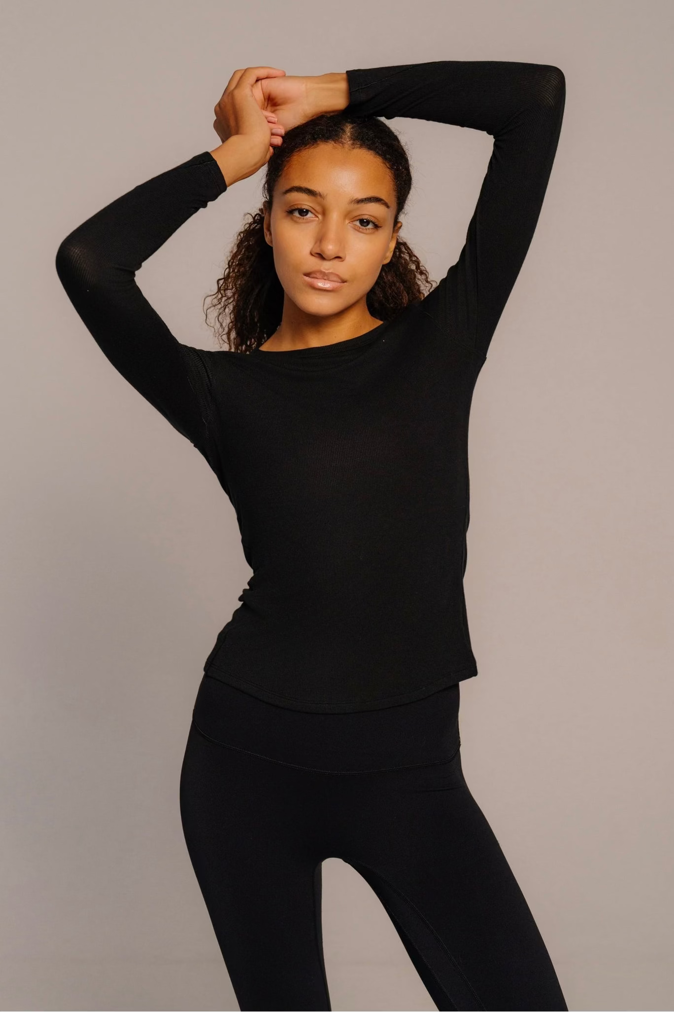 Person wearing a black long-sleeve top and pants against a plain background