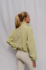 Woman wearing a light green sweatshirt and beige pants against a plain background