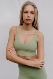 Woman wearing a green sports bra and leggings against a plain background