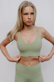Woman wearing a green sports bra and leggings against a plain background