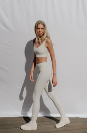 Woman wearing a beige sports bra and leggings standing against a white background
