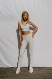 Woman wearing a white sports bra and leggings standing against a plain background
