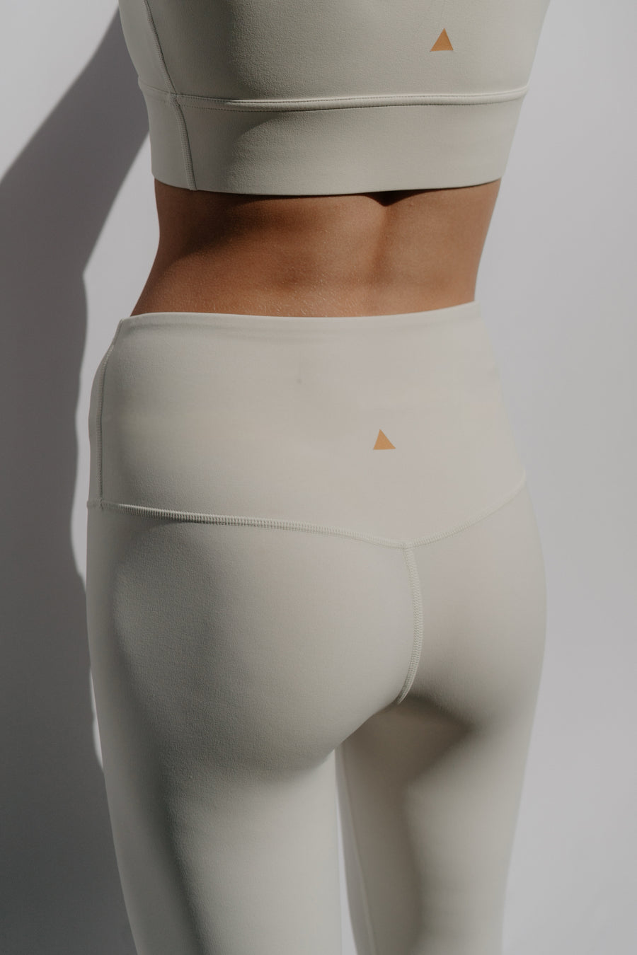 Ivory athletic leggings with a small triangle logo on a plain background