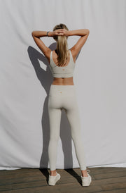 Woman wearing a sports bra and leggings against a plain background