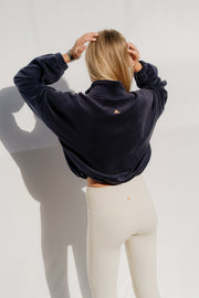 Woman wearing a navy blue sweatshirt and beige pants against a white background