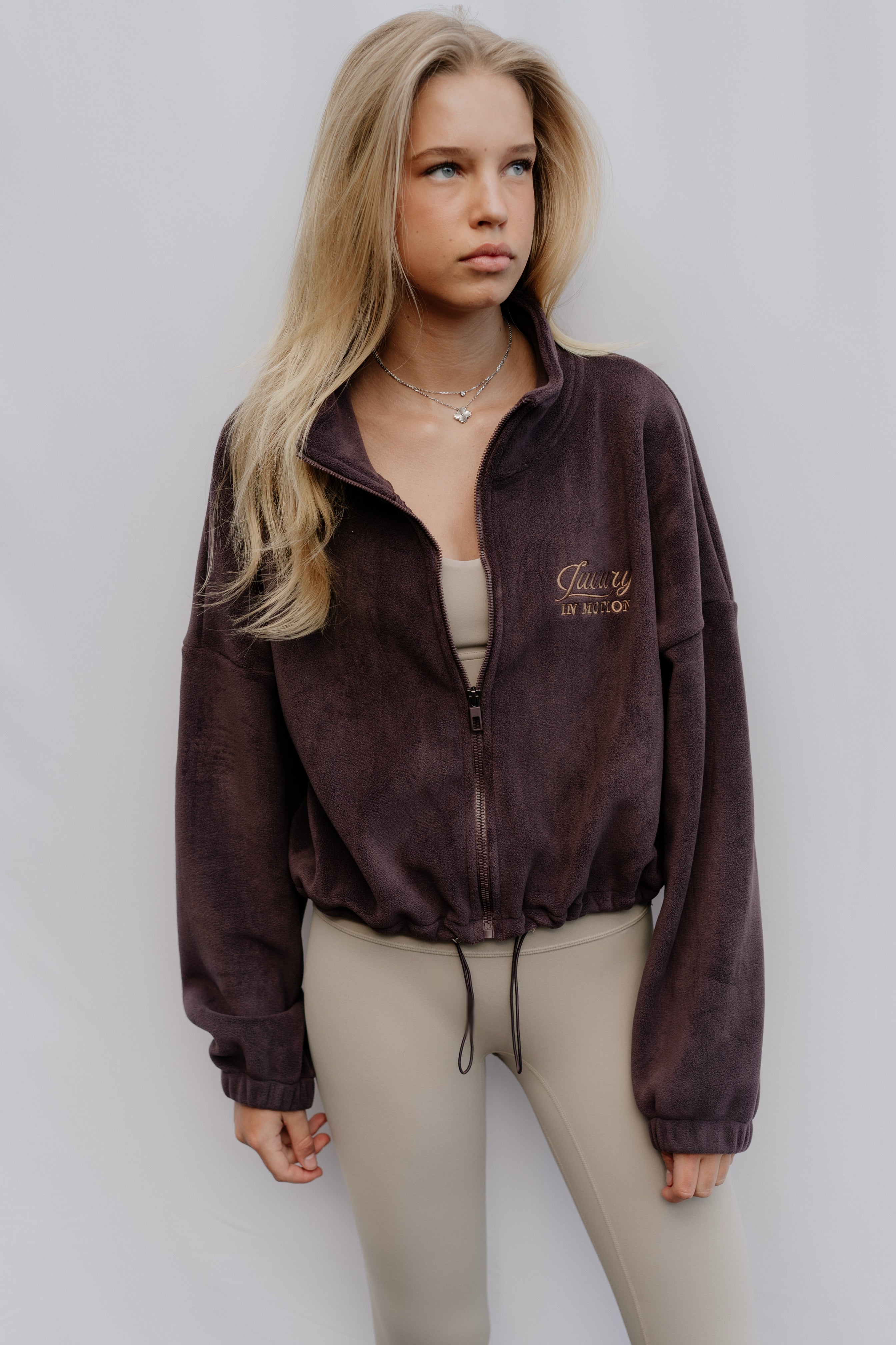 Woman wearing a brown jacket with a logo on a plain background