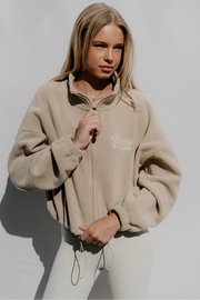Woman wearing a beige jacket with a logo on a plain background